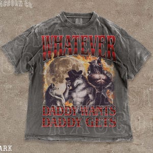 May include: Dark grey t-shirt featuring a graphic of three werewolves against a full moon backdrop. The text "WHATEVER" in red plaid lettering is above the image, with "DADDY WANTS DADDY GETS" below. The tee has a vintage, distressed appearance.