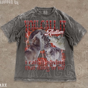 May include: Dark grey t-shirt with a graphic of three wolves howling at the moon, with the text "YOU CALL IT Autism, I call it having that dawg in me". The shirt is from "THE SILLY RACCOON CO".