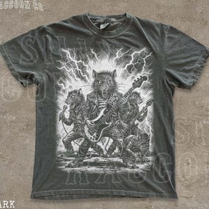 May include: Dark grey t-shirt featuring a black and white illustration of a rock band composed of anthropomorphic rats playing instruments. The text "THE SILLY RACCOON CO" and "DARK GREY" are printed on the shirt.