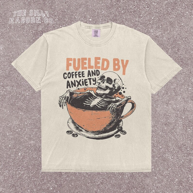 Funny coffee shirt for anxious introverts, featuring a skeleton relaxing in a giant coffee cup with the text “Fueled by Coffee and Anxiety.” Vintage grunge design with distressed print and muted tones. Ideal for women, men, and non-binary adults who love dark humor and caffeine culture. Great for Halloween, work-from-home vibes, mental health awareness, or gifting your favorite goth coffee lover.