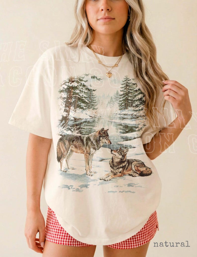 A woman wearing a white t-shirt with a graphic design of two wolves in a snowy forest.