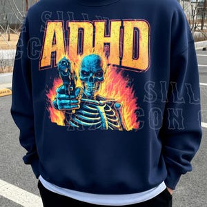 A navy blue sweatshirt with a graphic design depicting a skeleton holding a gun, with flames behind the skeleton.