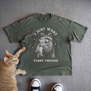 Vintage style Dark Grey t-shirt featuring grayscale illustration of friendly raccoon hugging cat surrounded by stars with I Just Want Furry Friends text, perfect for animal lovers and wildlife enthusiasts seeking whimsical, unique graphic tees