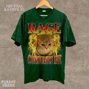 A green t-shirt with a graphic design featuring a cat's face surrounded by flames and the text "RAGE CONSUMES ME" printed on it.