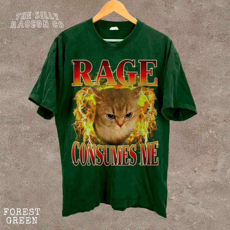 A green t-shirt with a graphic design featuring a cat's face surrounded by flames and the text "RAGE CONSUMES ME" printed on it.