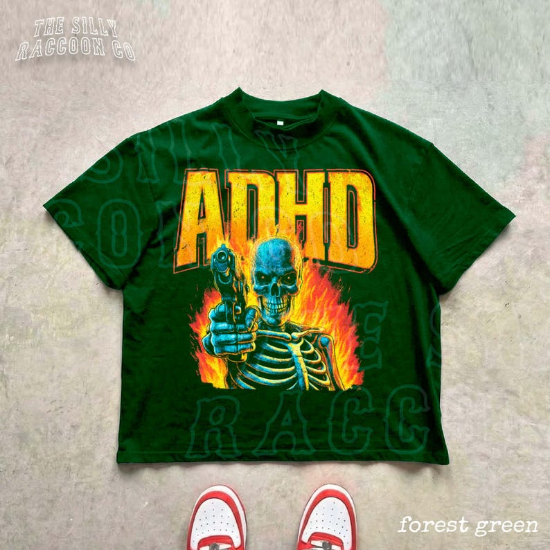 a green t-shirt with a graphic design depicting a skeleton holding a gun, with flames and text surrounding the image.