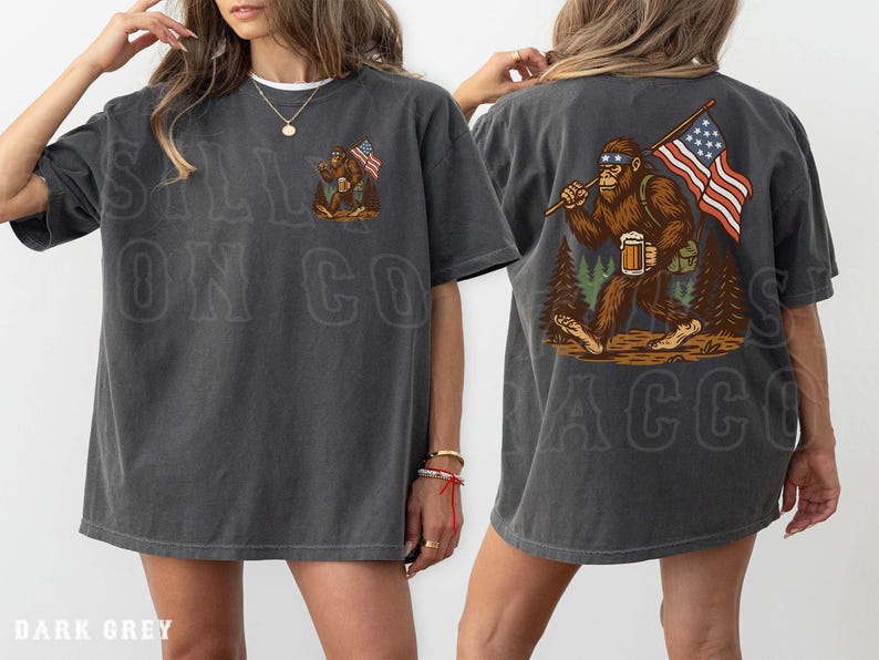 K&ouml;nnte beinhalten: Dunkelgraues T-Shirt mit einem Bigfoot-Motiv, das eine amerikanische Flagge und ein Bier h&auml;lt. Auf der Vorderseite des Shirts steht der Text "SALL ON CO". Auf der R&uuml;ckseite des Shirts befindet sich eine gr&ouml;&szlig;ere Bigfoot-Grafik mit der amerikanischen Flagge und Bier. Das Shirt hat eine lockere Passform.