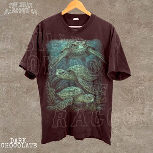 A dark brown t-shirt with a graphic design depicting three green sea turtles swimming underwater.