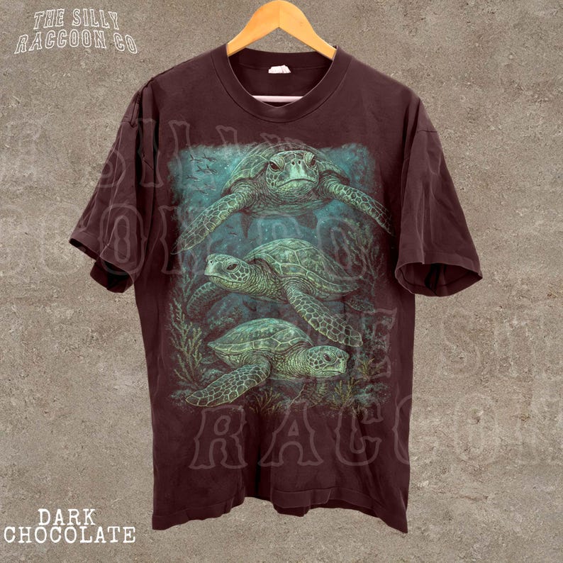 A dark brown t-shirt with a graphic design depicting three green sea turtles swimming underwater.