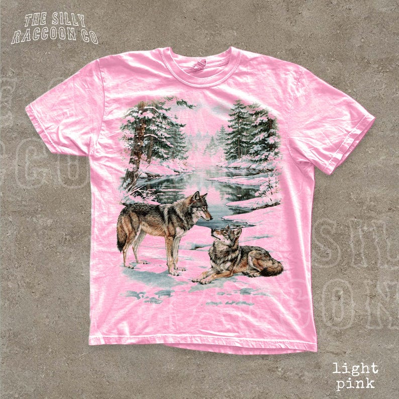 A pink t-shirt with a printed design depicting two wolves in a snowy forest landscape.