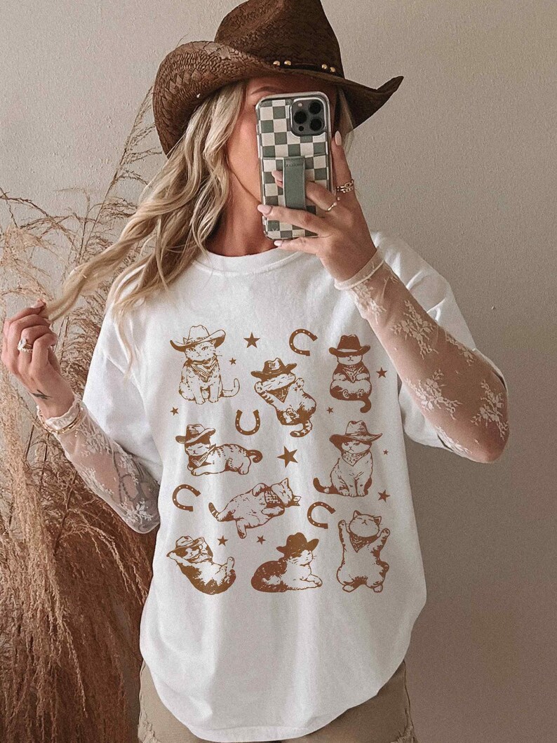 Vintage cowboy cat shirt for men and women featuring whimsical feline rodeo illustrations. Western-themed graphic t-shirt with cute kittens wearing cowboy hats, surrounded by horseshoes and stars. Soft, breathable fabric with a rustic, slightly distressed print for a retro aesthetic. Perfect for cat lovers, Western fashion enthusiasts, rodeo fans, and country music lovers. Unique gift idea for birthdays, holidays, or anyone who loves funny cat tees.