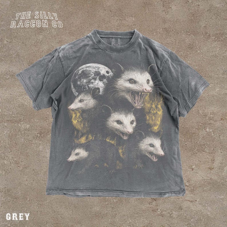 A grey t-shirt with a graphic design featuring multiple opossum faces with open mouths, arranged in a stacked formation.