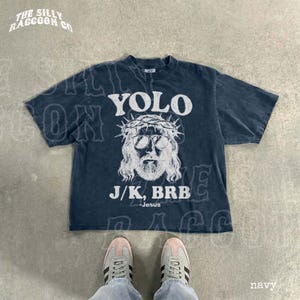 A navy blue t-shirt with a graphic design and text printed on it, along with a pair of sneakers and a person's feet.