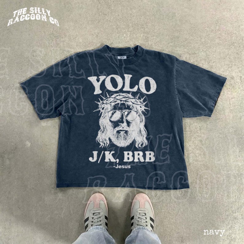 A navy blue t-shirt with a graphic design and text printed on it, along with a pair of sneakers and a person's feet.