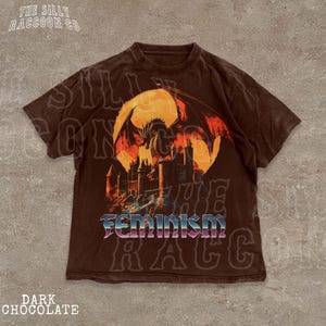 A brown t-shirt with a graphic design depicting a dragon and a castle, along with the word "Feminism" printed on it.