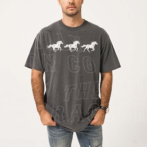 A man wearing a gray t-shirt with a graphic design of three horses running.