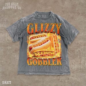 A grey t-shirt with a graphic design featuring two hot dogs on a flame background, along with the text "GLIZZY GOBBLER" prominently displayed.