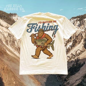 a t - shirt with a bigfoot holding a fish