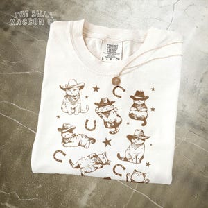a white t - shirt with a picture of a cat wearing a cowboy hat and