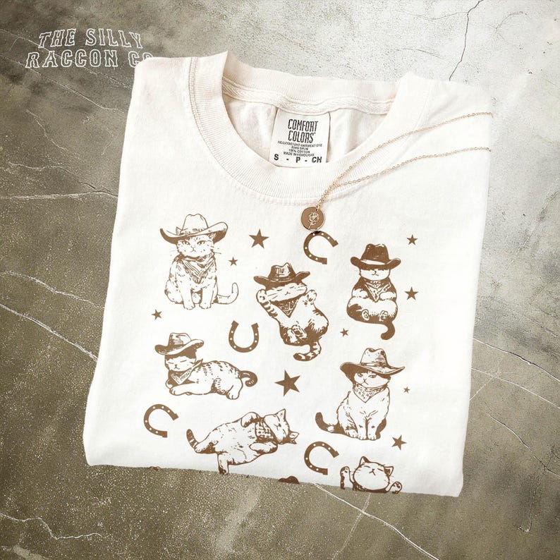 a white t - shirt with a picture of a cat wearing a cowboy hat and