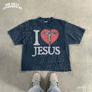 A navy blue t-shirt with a graphic of a cross and the text "I I heart JESUS" printed on it, along with a graphic of a person's feet wearing sneakers.