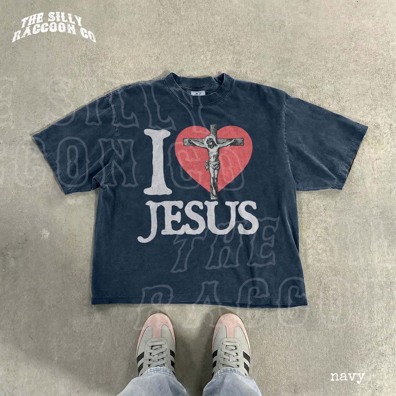 A navy blue t-shirt with a graphic of a cross and the text "I I heart JESUS" printed on it, along with a graphic of a person's feet wearing sneakers.