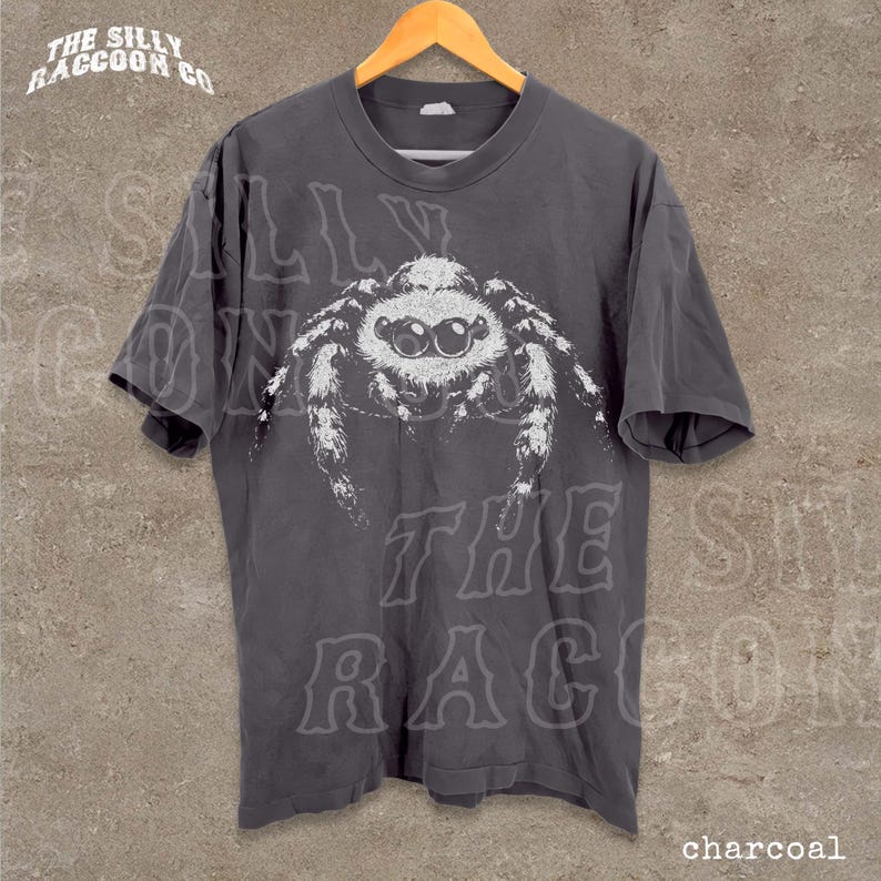 A gray t-shirt with a large white spider graphic printed on it, hanging on a wooden hanger.