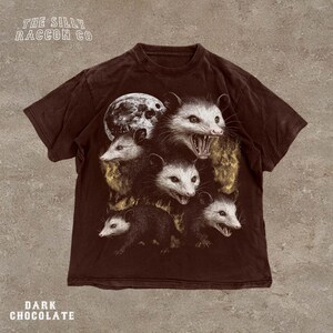 A dark brown t-shirt with a graphic design featuring multiple opossum faces with open mouths, creating a striking and visually captivating image.