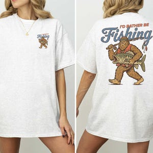 A woman wearing a white t-shirt with a graphic design of a fishing giant on the back.