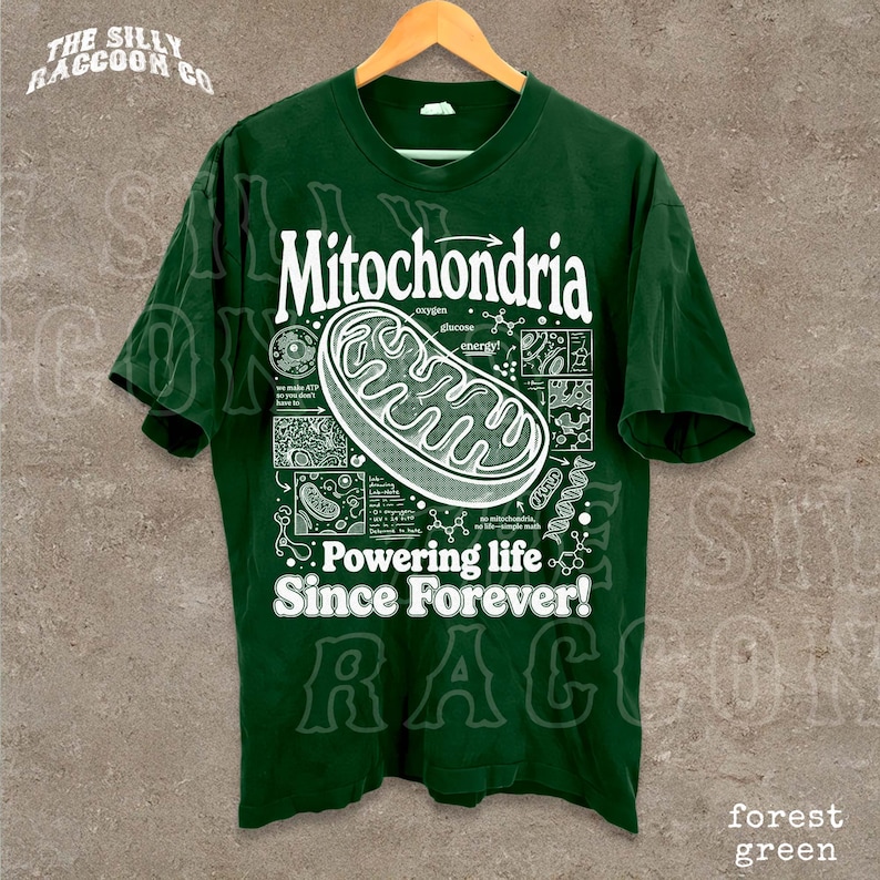 A green t-shirt with a graphic design depicting Mitochondria, a cellular organelle, and text that reads "Mitochondria. Powering life since forever!"