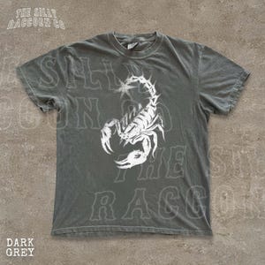 A gray t-shirt with a white graphic of a scorpion printed on it.