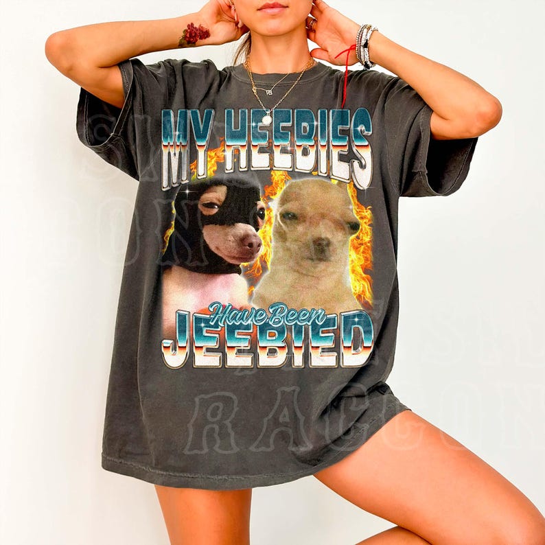 A person wearing a black t-shirt with a graphic design featuring two dogs and the text "MY HEEDIES HAVE BEEN JEEBIED" printed on it.