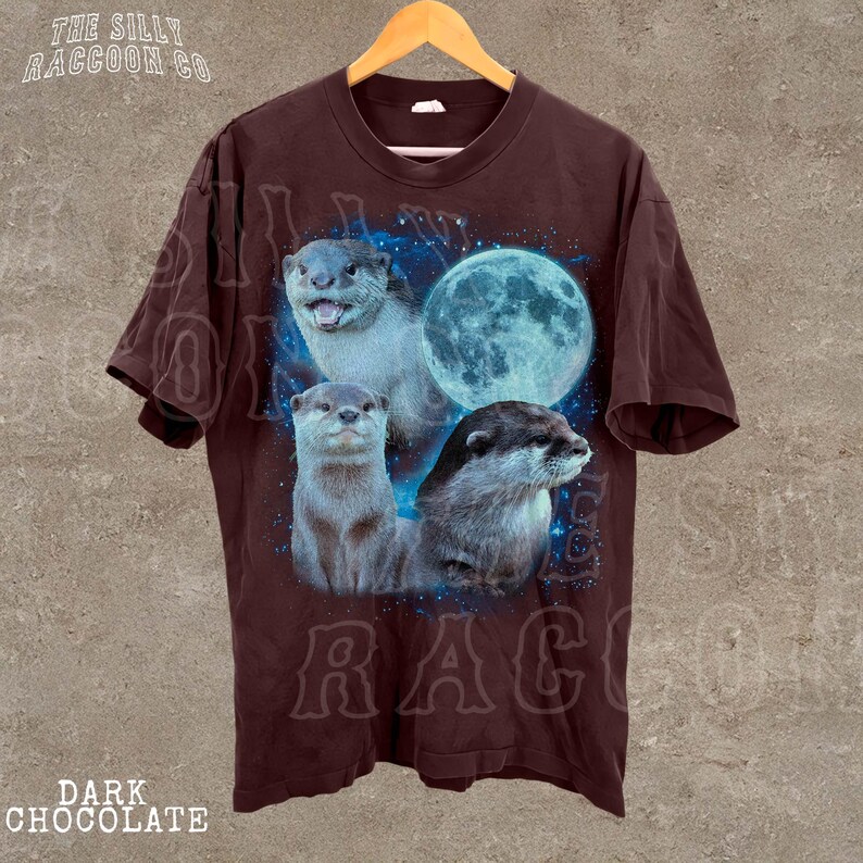 A brown t-shirt with a graphic design featuring three otters against a backdrop of a full moon and blue stars.