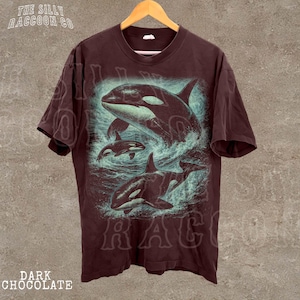 A dark brown t-shirt with a graphic design depicting two orca whales swimming in the ocean.