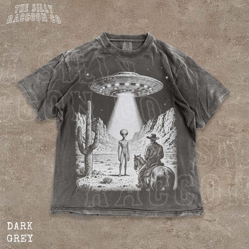 The image is a t-shirt design featuring a scene with an alien spacecraft hovering above a desert landscape, where a man on a horse is present.