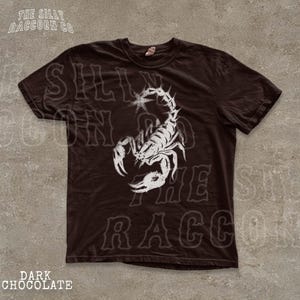 A dark brown t-shirt with a white graphic design depicting a stylized scorpion.
