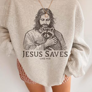A person wearing a gray sweatshirt with a graphic of Jesus holding a raccoon printed on it.