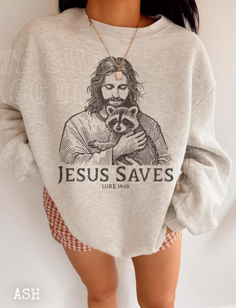 A person wearing a gray sweatshirt with a graphic of Jesus holding a raccoon printed on it.