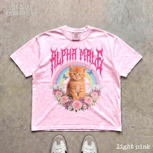 A pink t-shirt with a graphic design featuring an orange cat, a rainbow, and flowers.