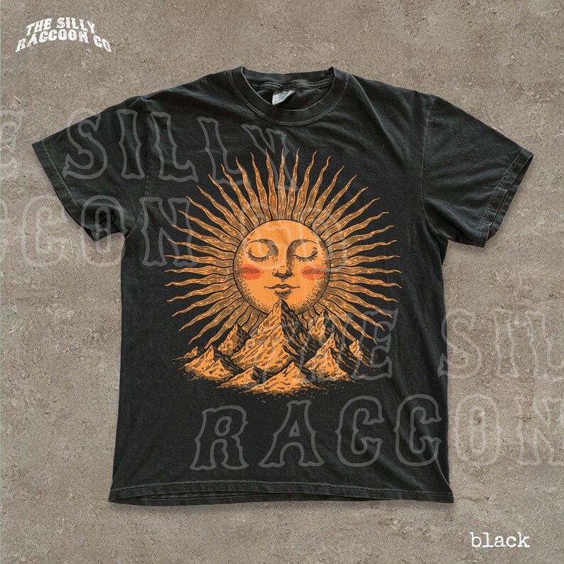 A black t-shirt with a graphic design depicting a sun with rays emanating from it, surrounded by mountains.