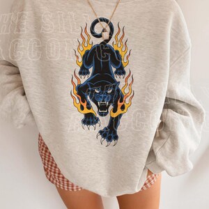 A person wearing a grey sweatshirt with a graphic design of a black panther with flames on its back.