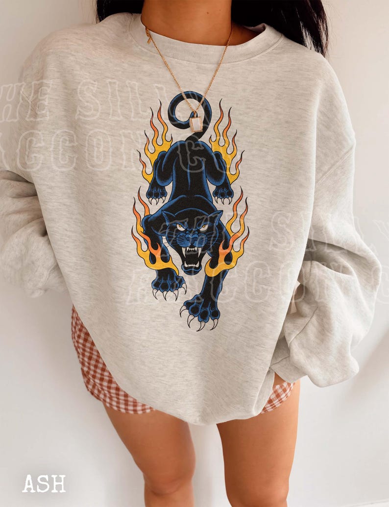 A person wearing a grey sweatshirt with a graphic design of a black panther with flames on its back.