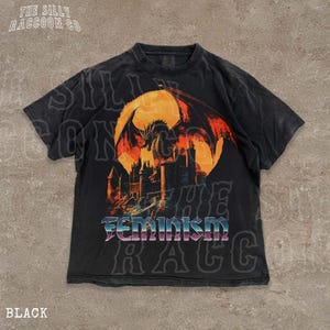 A black t-shirt with a graphic design depicting a dragon and a castle, along with the word "Feminism" printed on it.