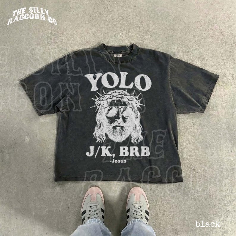A black t-shirt with a graphic design and text printed on it, along with a pair of sneakers and a person's feet.