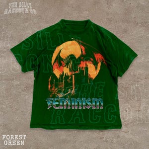 A green t-shirt with a graphic design depicting a dragon and a castle, along with the word "Feminism" printed on it.
