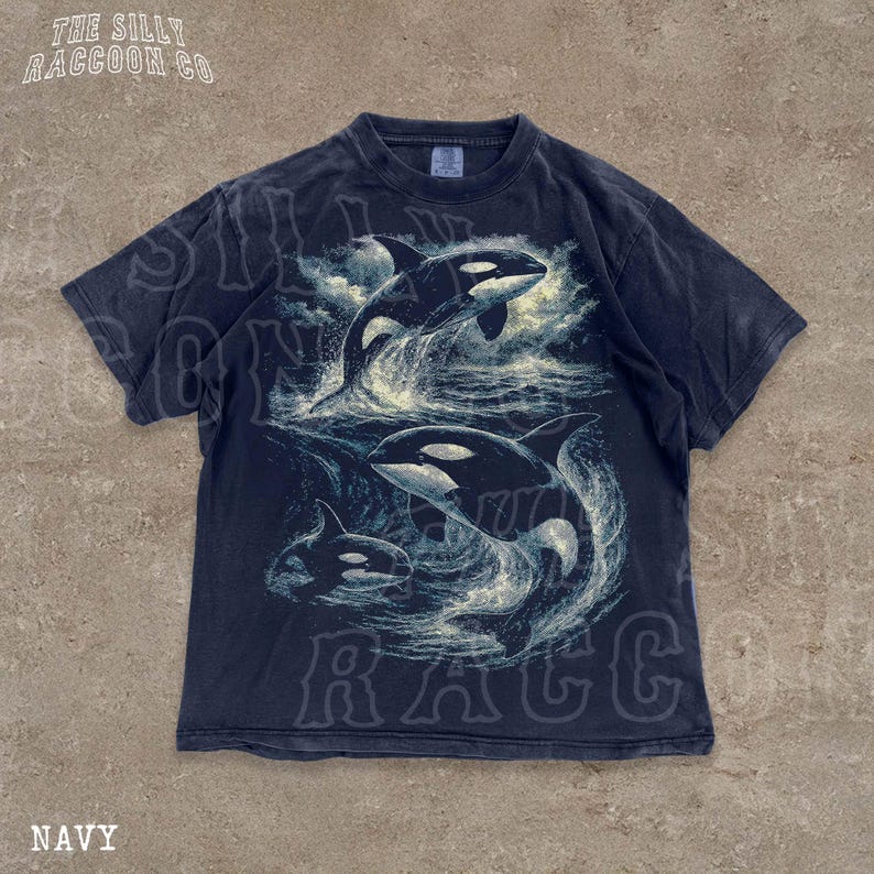 A navy blue t-shirt with a graphic design depicting two orca whales in the ocean.
