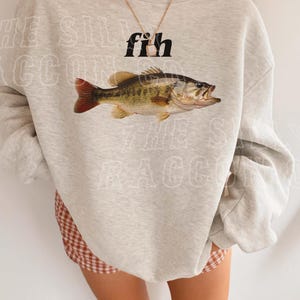 A person wearing a grey sweatshirt with a fish graphic and a necklace.
