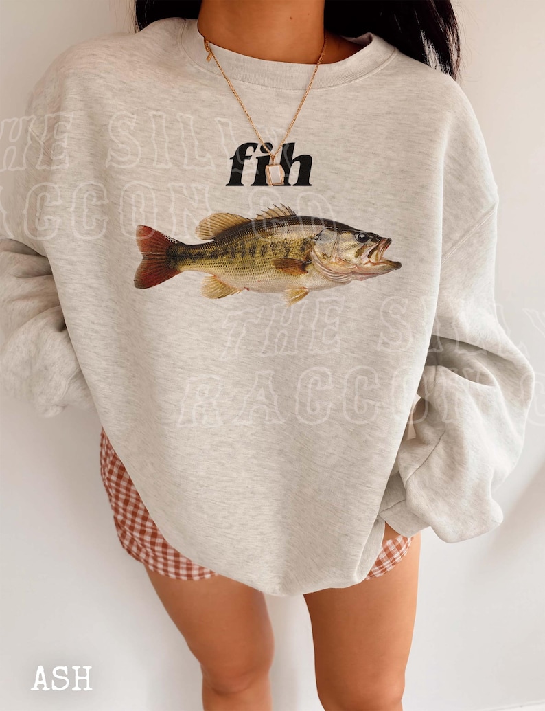 A person wearing a grey sweatshirt with a fish graphic and a necklace.