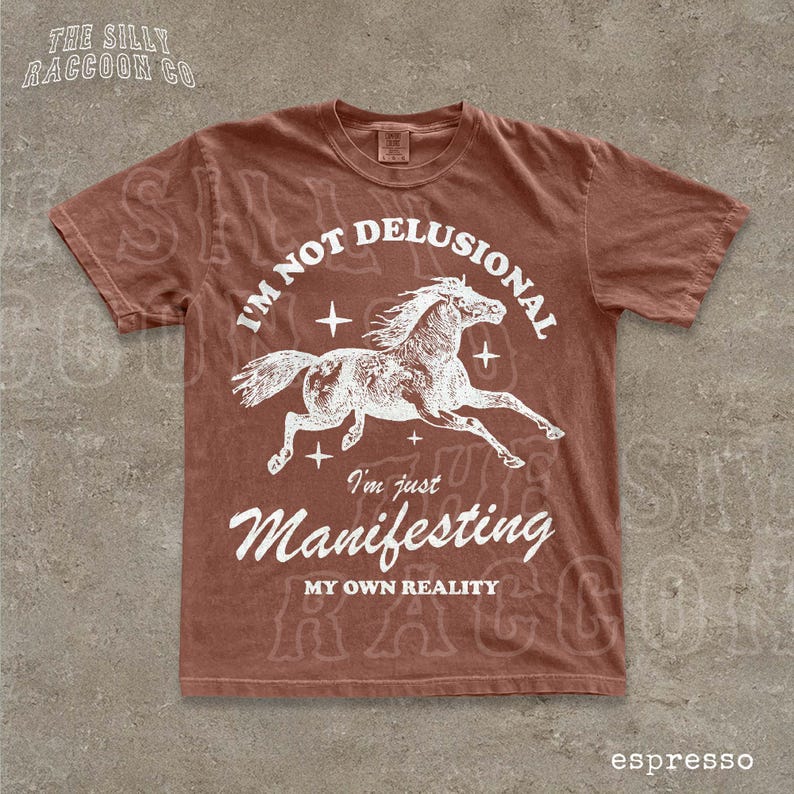 a brown t-shirt with a graphic design of a horse and the text "I'm not delusional, I'm just Manifesting my own reality" printed on it.