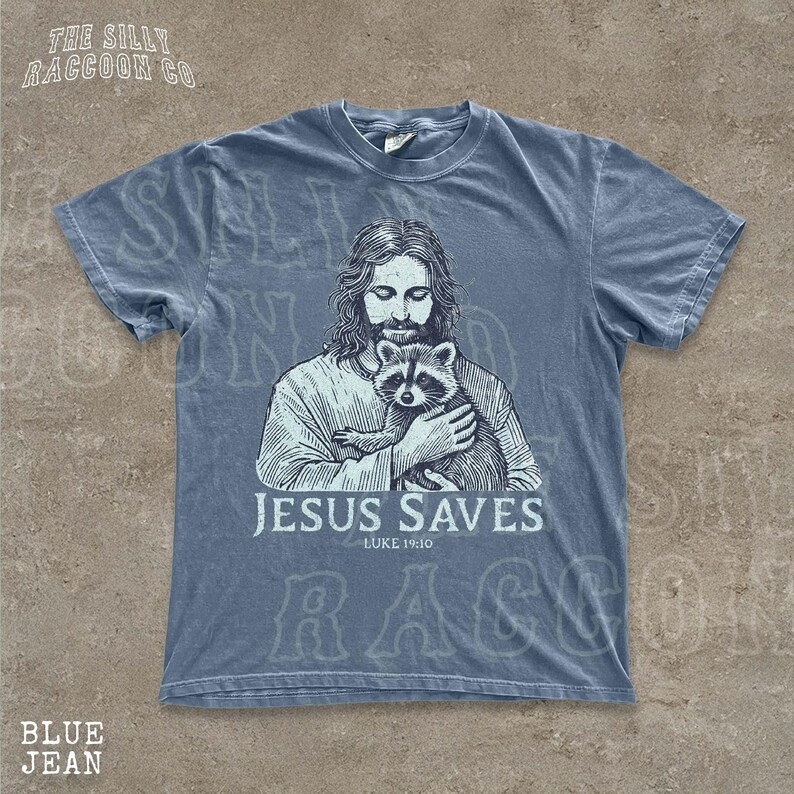 A t-shirt design featuring an illustration of Jesus holding a raccoon, with the text "JESUS SAVES" and "LUKELINE 1910" printed on it.